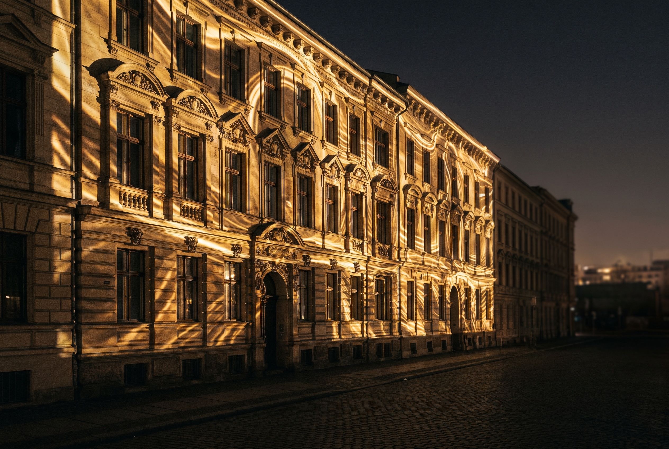 Gründerzeit-Altbaufassade mit Stuckornamenten, nachts in warmes Gold-Licht getaucht